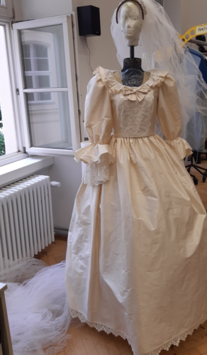 Schaufensterpuppe trägt ein cremefarbenes Brautkleid mit Puffärmeln, Spitze und einer langen, weißen Schleppe im hellen Raum.