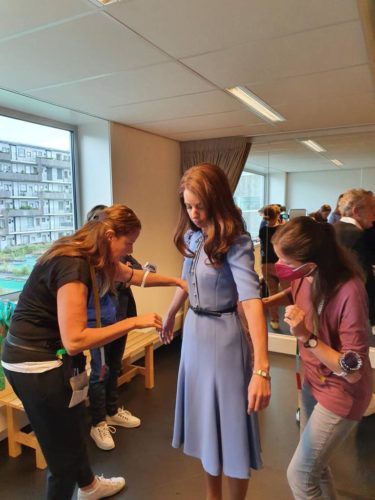 Eine Frau in einem blauen Kleid wird von zwei anderen Frauen für eine Anprobe oder Anpassung vorbereitet.