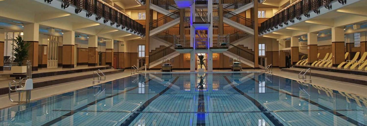 Großes, elegantes Hallenbad mit zwei Etagen, Liegestühlen und einer breiten Treppe im Hintergrund.