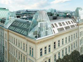 Historisches Gebäude mit modernem Glasdach und mehreren Oberlichtern, Stadtansicht im Hintergrund.