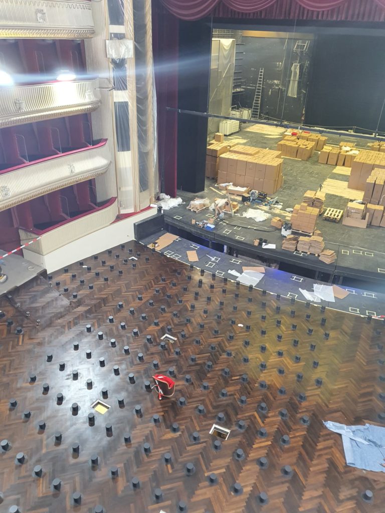 Blick in ein Theater mit abgedeckten Sitzen und vielen Umzugskartons und Werkzeugen auf der Bühne, Renovierungsarbeiten finden statt.