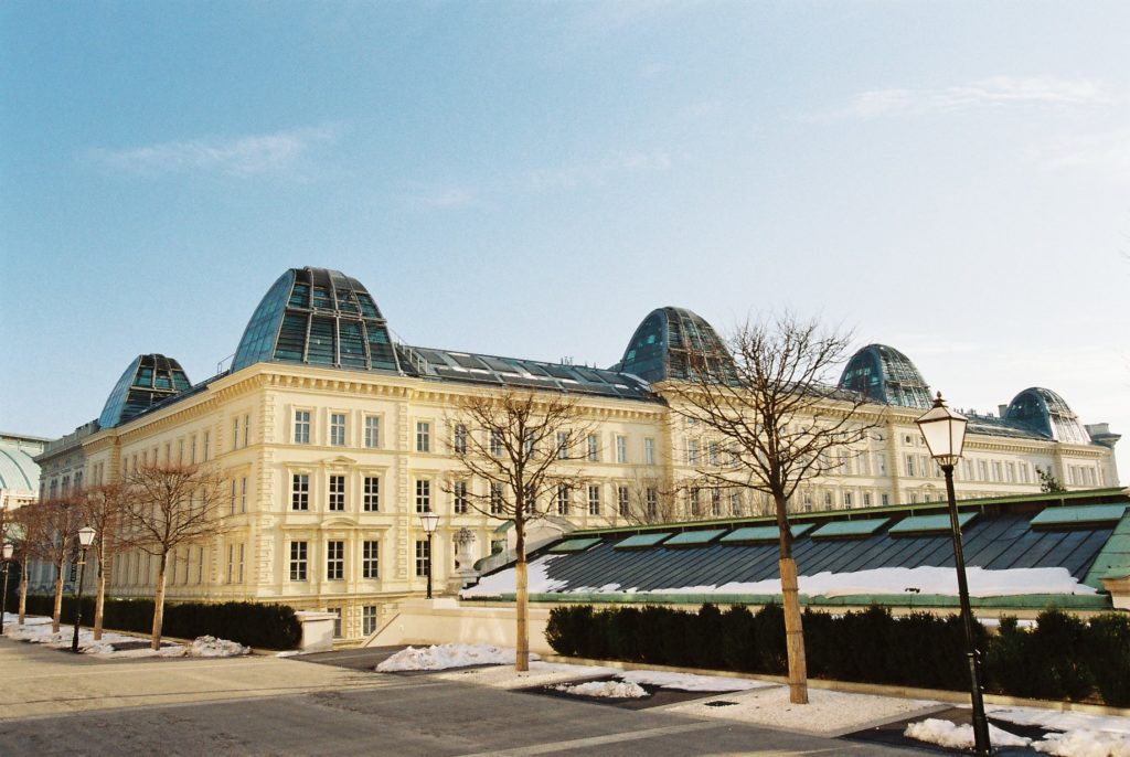 Großes, helles Gebäude mit modernen Glasdächern, umgeben von kahlen Bäumen, Schnee und Straßenlaternen bei klarem Himmel.