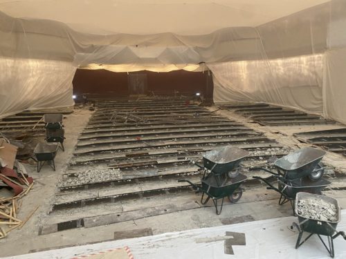 Baustelle in einem mit Plastikfolie abgehängten Raum, Holzbalken am Boden und mehrere Schubkarren voller Schutt.