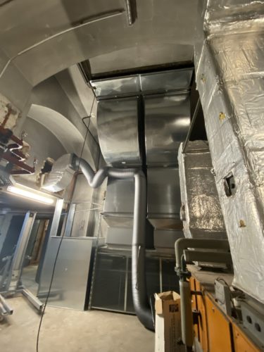 Große Belüftungsanlage mit silbernen Lüftungskanälen und isolierten Rohren in einem Technikraum.