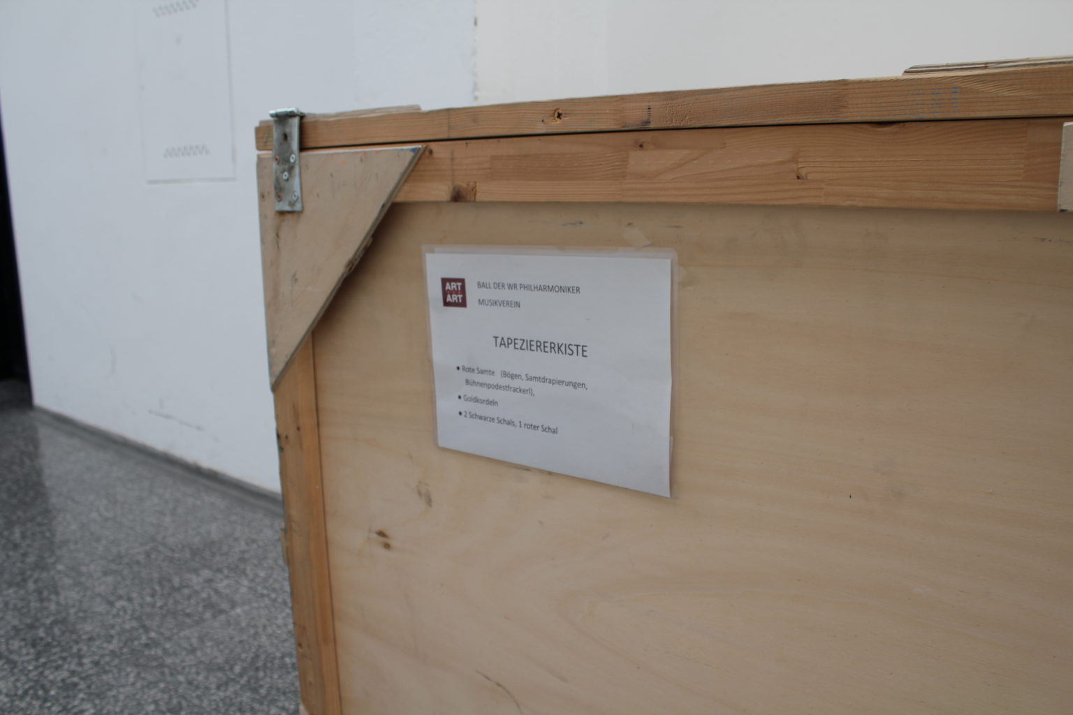 Holzkiste mit einem Schild, auf dem „Tapetenzierliste“ und eine kurze Aufzählung von Inhalten steht.