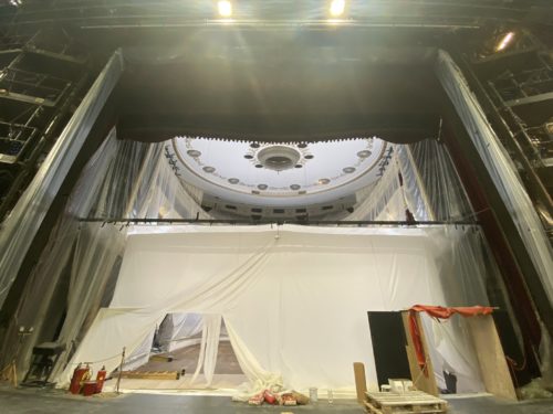 Blick auf eine Theaterbühne mit weißer Plastikplane als temporäre Wand, Bauutensilien und abgedeckter Decke.