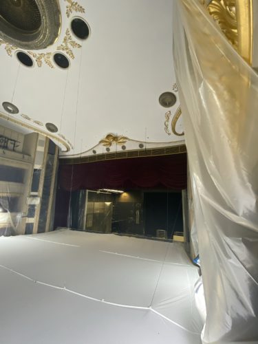 Blick in einen Theatersaal mit rotem Vorhang, goldenen Verzierungen und einer großen weißen Abdeckung auf dem Boden.