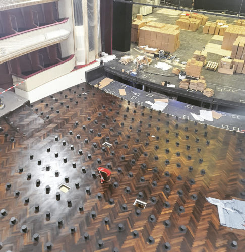 Blick auf eine Theaterbühne im Umbau, mit abgebautem Bühnenboden und vielen schwarzen Stiften sowie Kartons im Hintergrund.