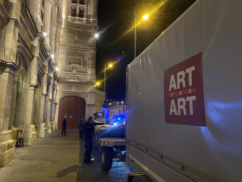 Ein Lastwagen mit dem Schriftzug „ART FOR ART“ steht nachts vor einem historischen Gebäude, daneben stehen mehrere Personen.