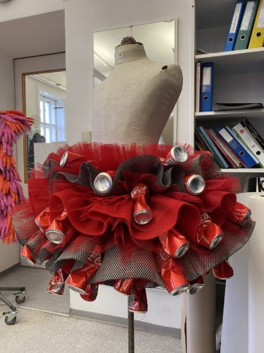 Eine Schneiderpuppe trägt einen Rock aus roten Coca-Cola-Dosen, rotem Tüll und schwarzem Netzstoff in einem Atelier.