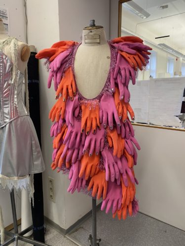 Schaufensterpuppe trägt ein auffälliges Kleid, das aus übereinander gelegten pinken und orangefarbenen Gummihandschuhen besteht.