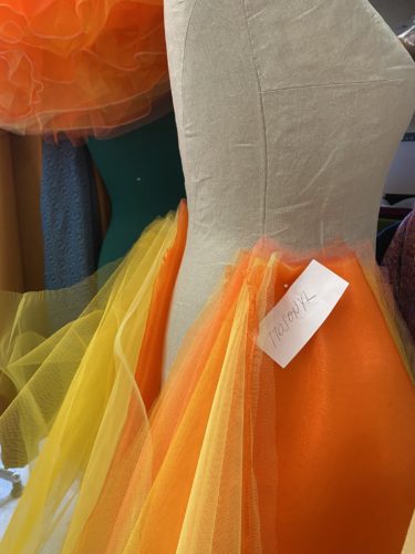 Eine Schneiderbüste mit orangem und gelbem Tüll, darauf ein Zettel mit handgeschriebener Notiz befestigt.