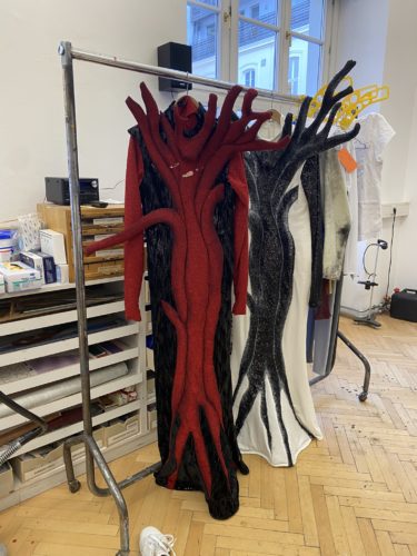 Zwei auffällige Kleider in Baumform, eines rot und eines schwarz-weiß, hängen an einer Kleiderstange in einem Atelier.