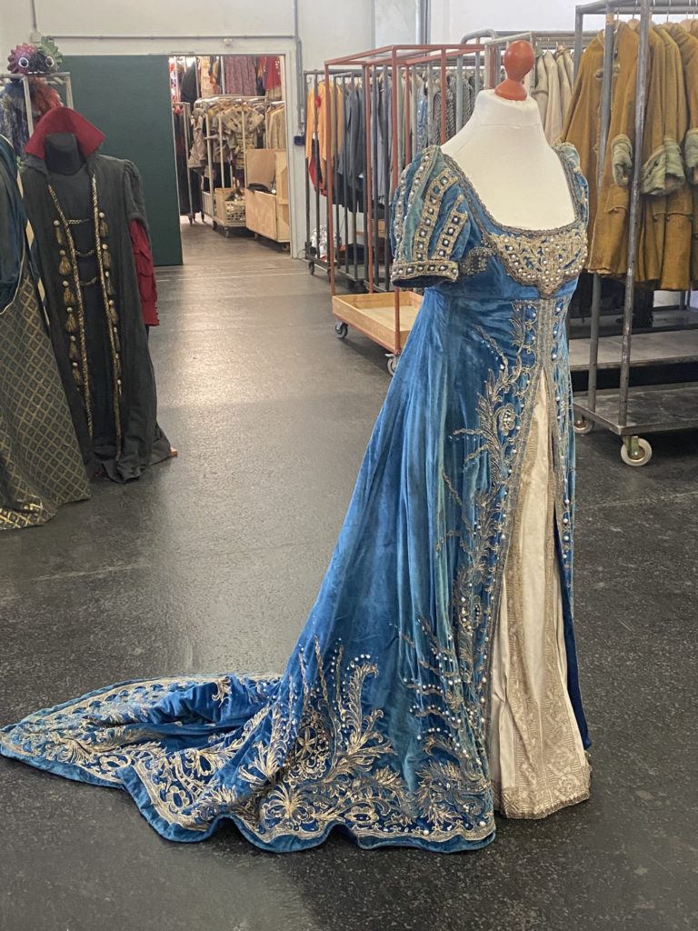 Ein aufwendiges, historisches blaues Kleid mit silbernen Verzierungen und einer langen Schleppe auf einer Schneiderpuppe.