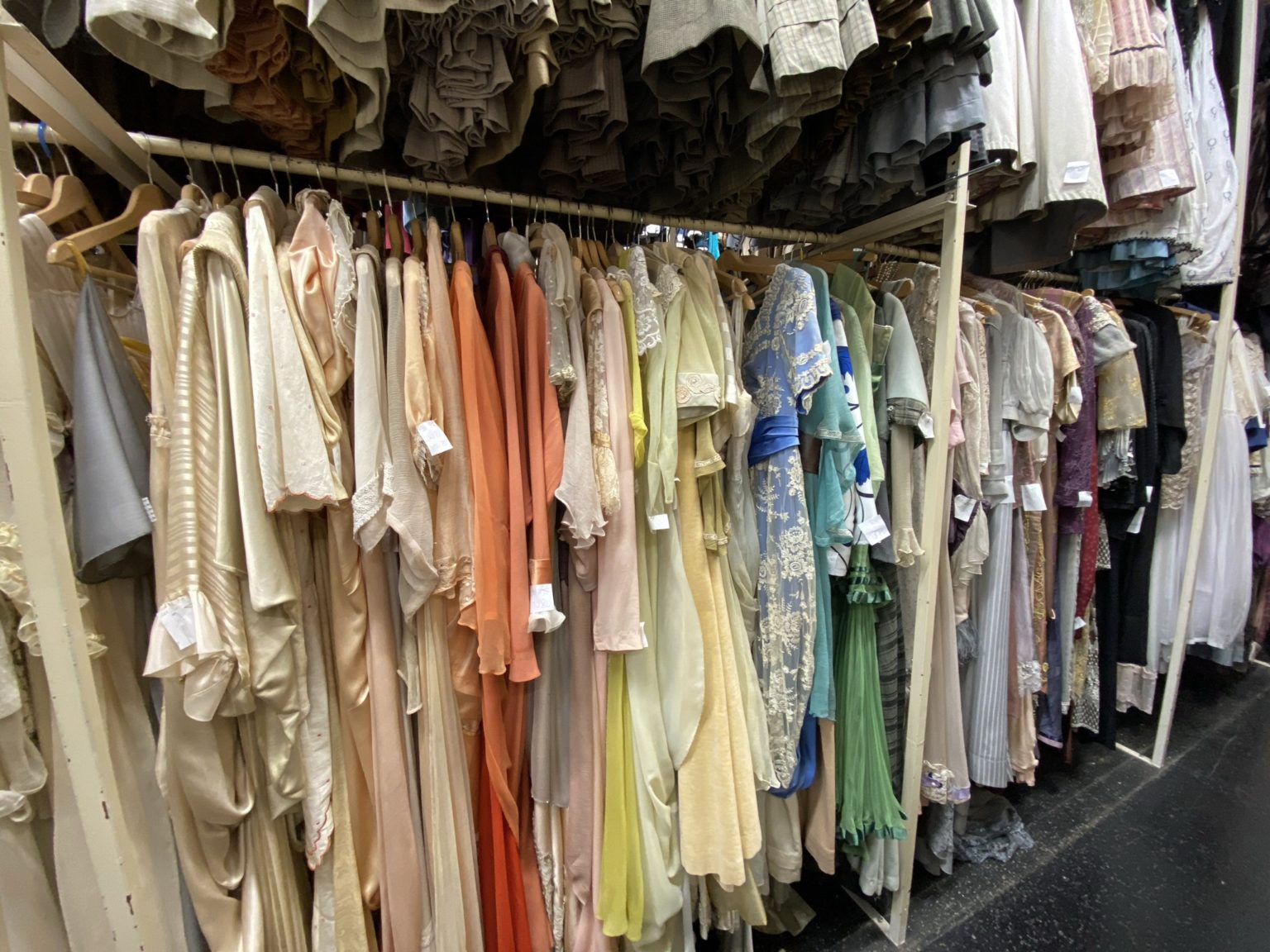 Eine Reihe von eleganten Kleidern in verschiedenen Pastellfarben hängt ordentlich auf Kleiderbügeln in einem Kleiderraum.