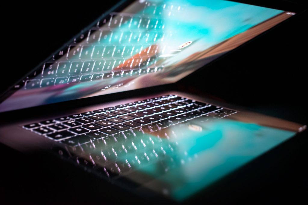 Eine aufgeklappte Laptop-Tastatur mit leuchtenden Tasten und einer spiegelnden Bildschirmreflexion.