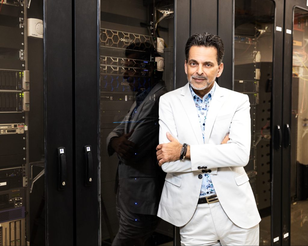 Ein Mann im weißen Anzug steht mit verschränkten Armen vor Server-Schränken in einem Rechenzentrum.