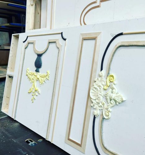 Dekorative Wandpaneele mit aufwendigen, teils goldfarbenen Stuckverzierungen und floralen Elementen in einer Werkstatt.