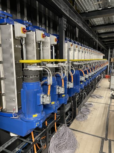 Mehrere große blaue Elektromotoren mit Verkabelung sind in einer Reihe in einer Industrieanlage montiert.