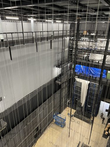 Ein Blick hinter die Bühne eines Theaters mit vielen Seilzügen, Technik und Arbeitsgeräten auf dem Bühnenboden.