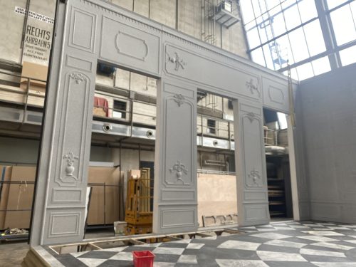 Eine große, graue Kulisse mit klassizistischen Ornamenten steht in einer Werkhalle mit hohen Fenstern und industrieller Umgebung.