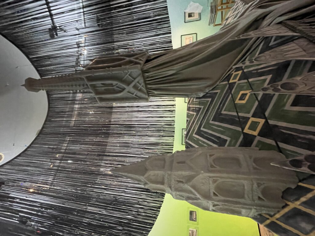 Zwei große, gotische Turmnachbildungen stehen in einem Raum mit grünlicher Wand und einer kunstvollen, dunklen Deckeninstallation.