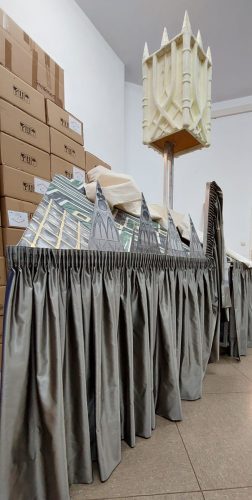 Mehrere Dekorationselemente, die an gotische Architektur erinnern, stehen hinter einem grauen Vorhang; im Hintergrund sind gestapelte Kartons zu sehen.