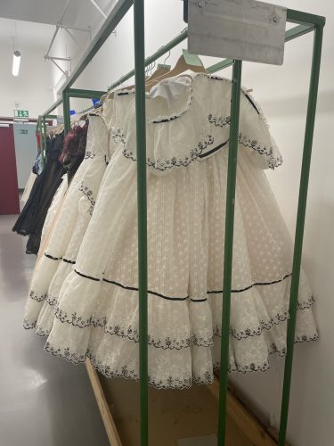 Weiße, weit ausgestellte Kleider mit Spitzen- und Stickereiverzierungen hängen auf Kleiderbügeln in einer Garderobe.