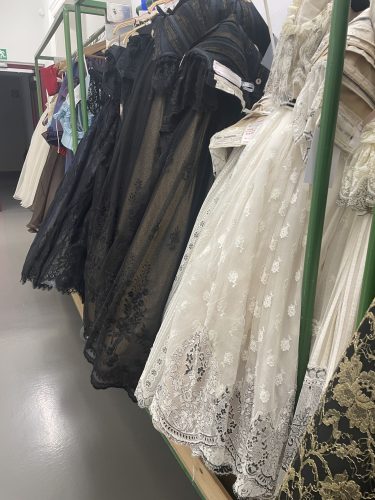 Reihe von eleganten Kleidern, darunter schwarze und cremefarbene Spitzenkleider, hängen ordentlich auf Kleiderbügeln.
