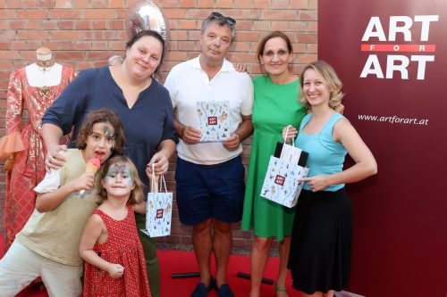Fünf Erwachsene und zwei Kinder mit bemaltem Gesicht posieren lachend vor einem ART FOR ART Banner mit Geschenktüten.