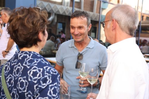 Drei Menschen unterhalten sich entspannt im Freien und halten jeweils ein Glas Weißwein in der Hand.