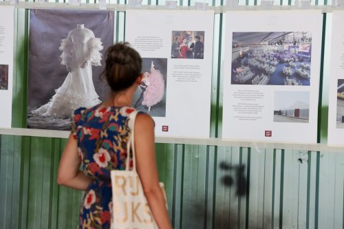 Eine Frau mit gemustertem Kleid und Stofftasche betrachtet Infotafeln und ein ausgestelltes weißes Kleid.