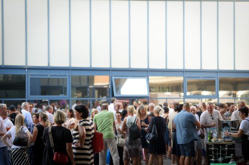 Viele Menschen unterhalten sich und stehen zusammen bei einer Veranstaltung im Freien vor einem modernen Gebäude.