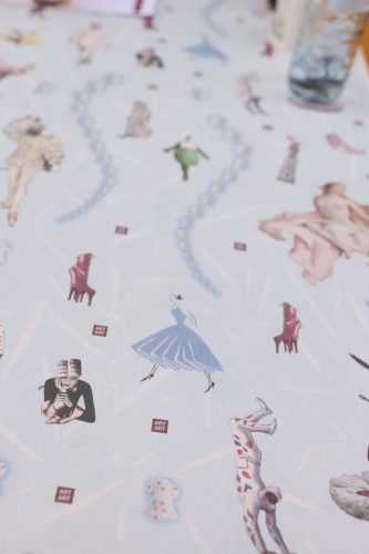 Tischdecke mit Illustrationen von Menschen in verschiedenen Posen und Outfits sowie kleinen Schriftzügen „ART“.