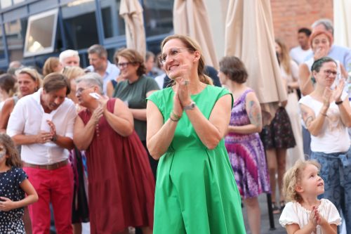 Frau in grünem Kleid klatscht und lächelt, während sie von weiteren applaudierenden und lachenden Menschen bei einer Feier umgeben ist.