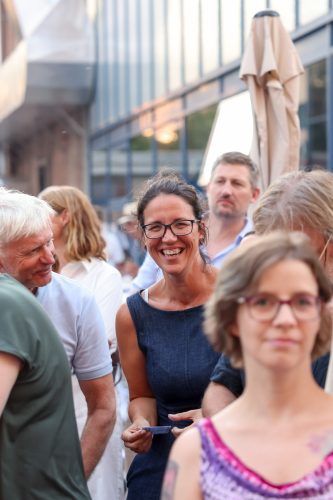 Mehrere Menschen unterhalten sich und lächeln auf einer belebten Outdoor-Veranstaltung bei Tageslicht.