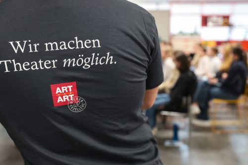 Rückenansicht einer Person mit einem T-Shirt, auf dem steht: "Wir machen Theater möglich." sowie das Logo von ARTE.