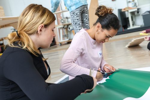 Zwei junge Frauen arbeiten gemeinsam an einem grünen Bastelprojekt auf dem Boden.