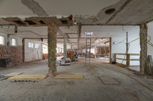 Große Baustelle in einem Gebäude mit freigelegten Wänden, Säulen, Baumaterialien und Baugeräten im Raum.