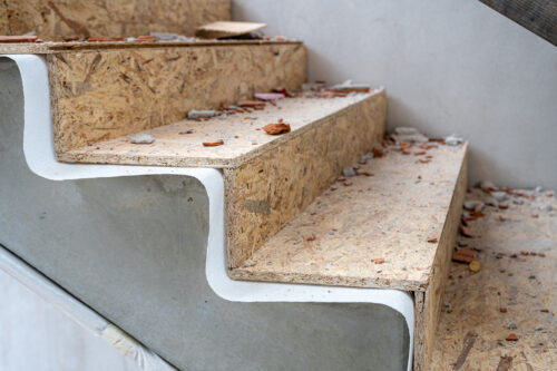 Eine Treppe aus Holzspanplatten mit Bauschutt und Staub auf den Stufen in einer unfertigen Umgebung.