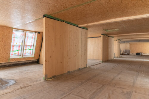 Eine Baustelle eines Holzhauses mit teilweise montierten Innenwänden, unverkleideten Fußböden und isolierten Fenstern.